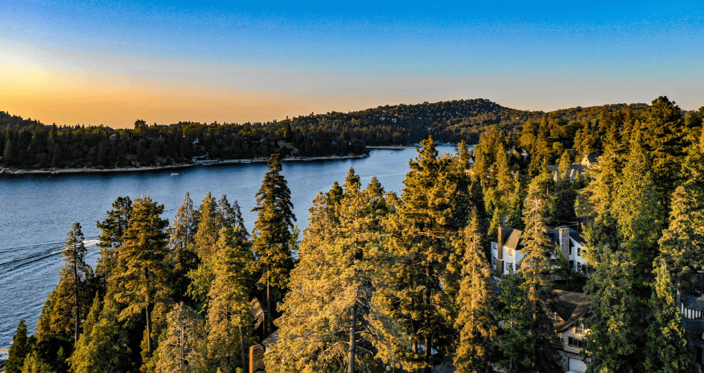 Aerial sunset view of Lake Arrowhead with blue water, green trees, boats, golden clouds, yellow, red, orange, blue, pink, purple colors