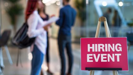 hiring event sign with people networking in a room